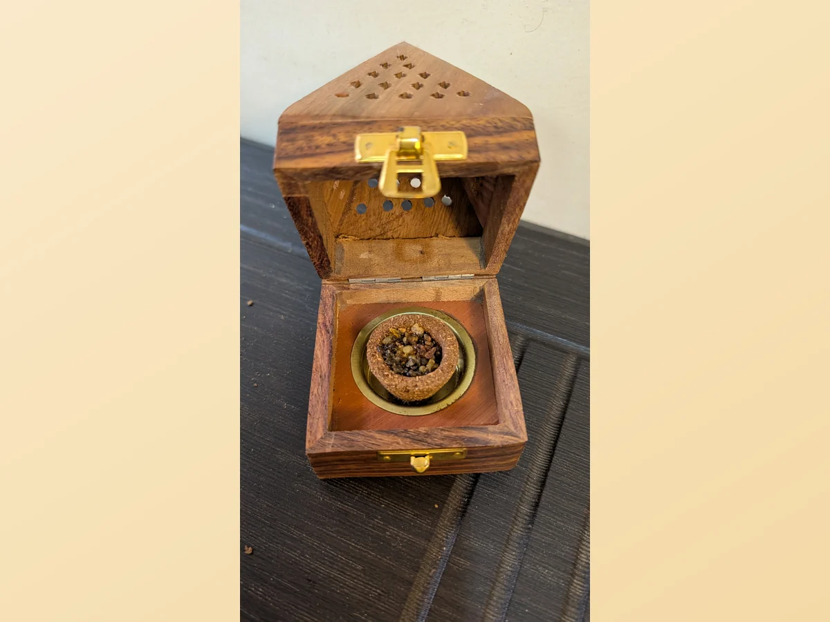 The pyramid holder open, a sambrani cup resting on the brass plate inside